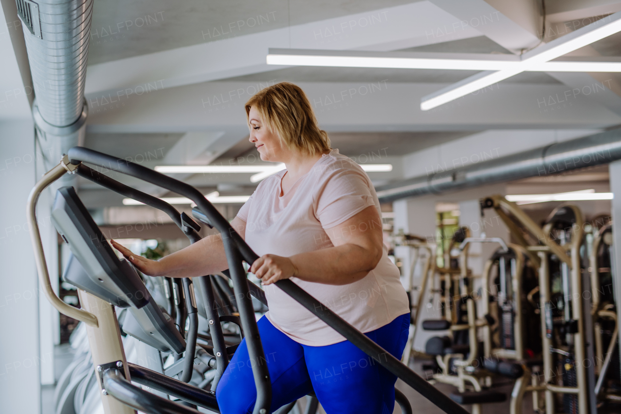 A happy mid adult overweight woman exercising on stepper indoors in gym