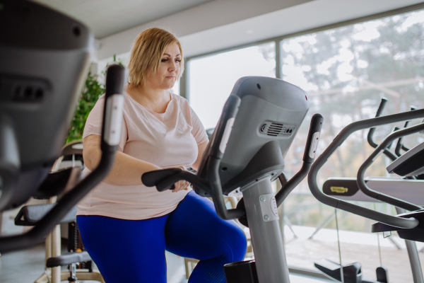 A happy mid adult overweight woman exercising on stepper indoors in gym