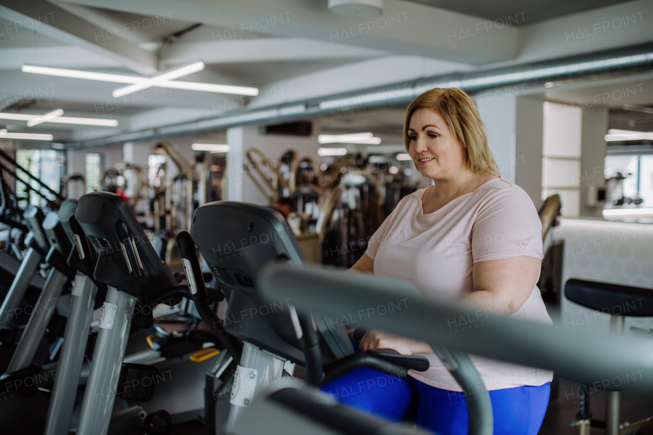 A happy mid adult overweight woman exercising on stepper indoors in gym