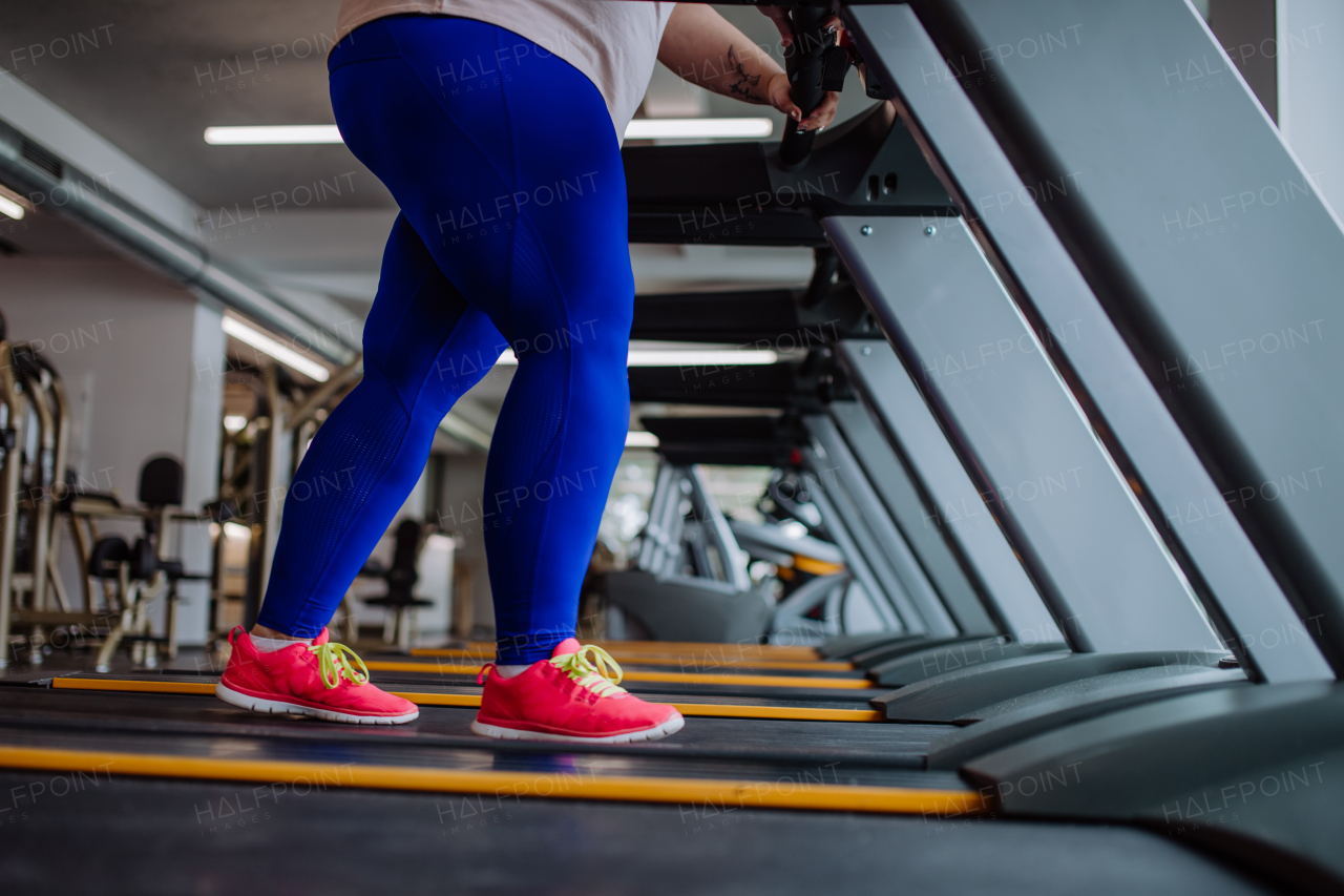 A low section of overweight woman with headphones exercising on treadmill in gym