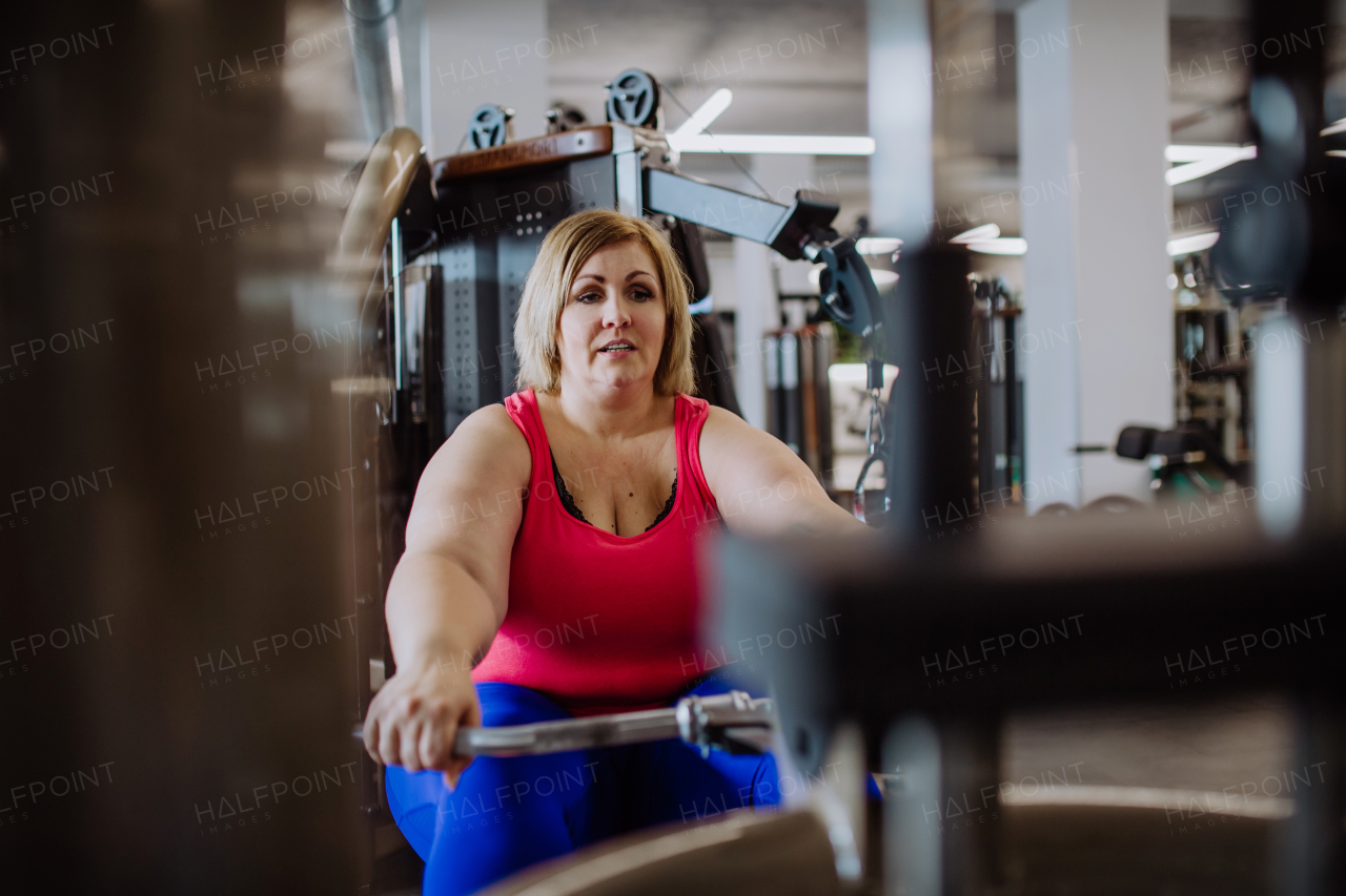 A plus size woman training on rowing machine indoors in gym