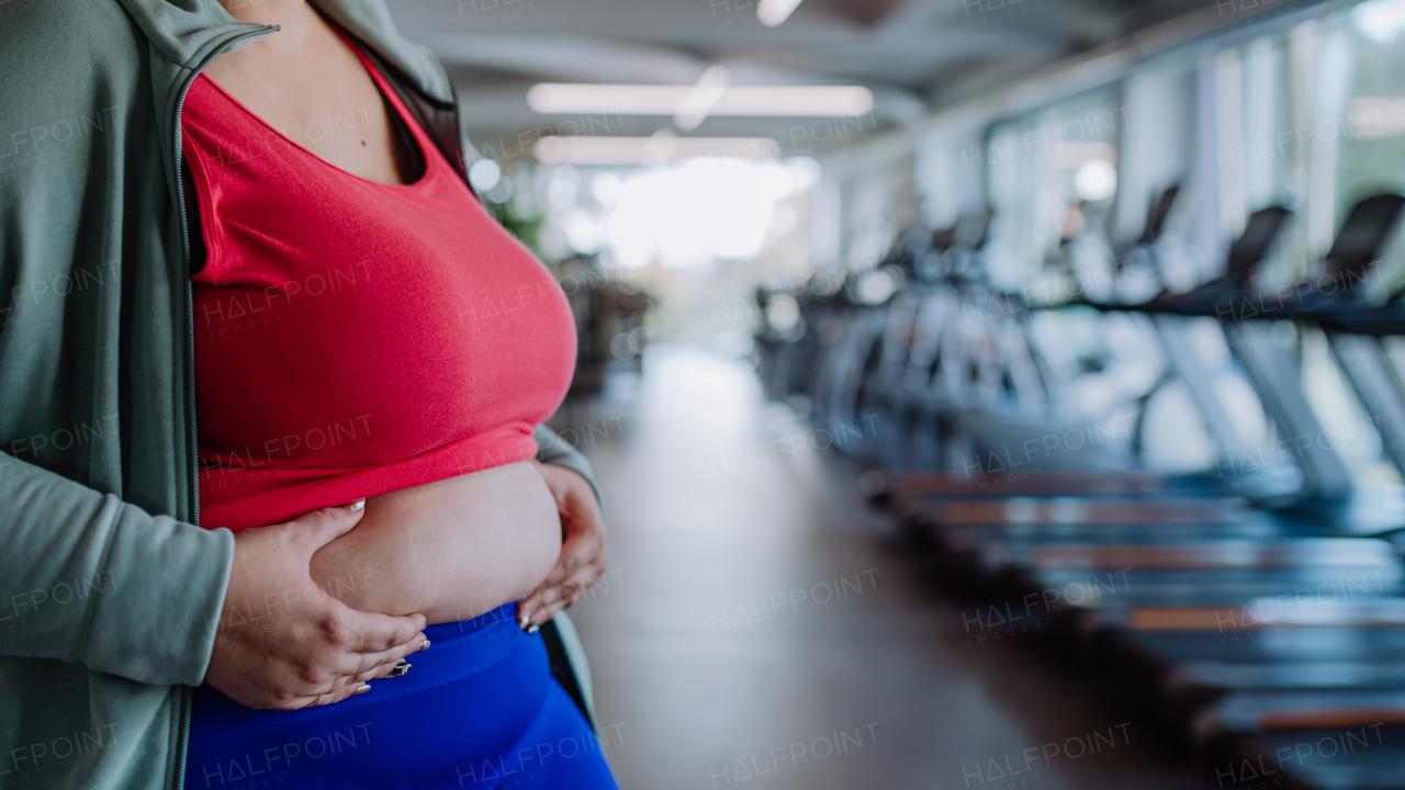 A midsection of overweight woman in sports clothes showing her excessive belly indoors in gym