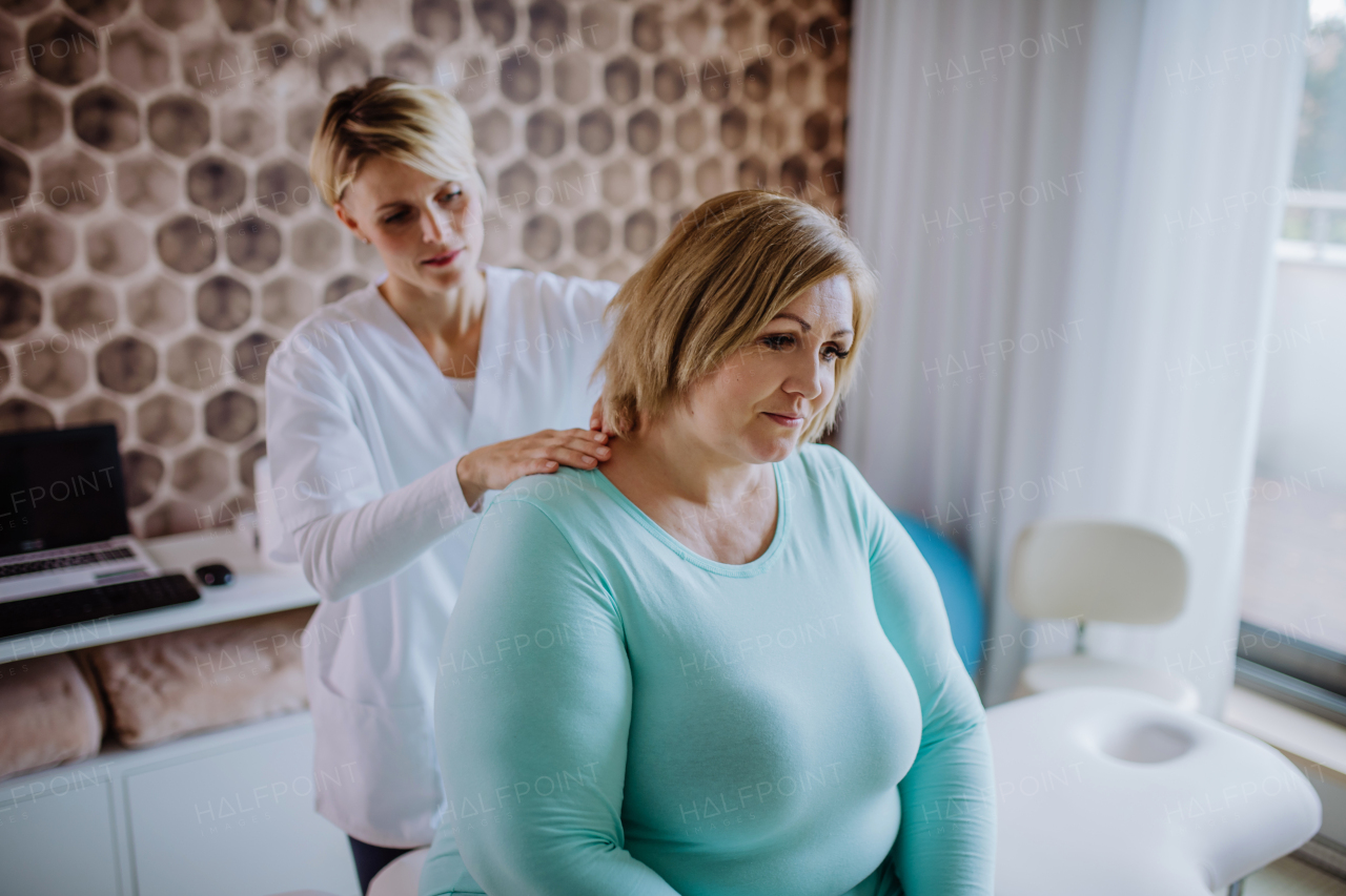 A mid adult physiotherapist woman exercising with overweight woman indoors in rehabilitation center