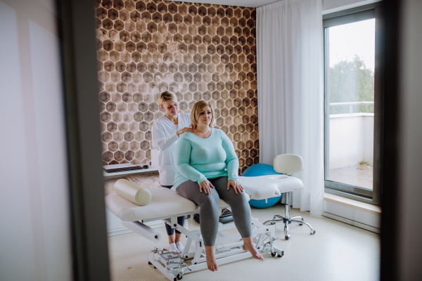 A mid adult physiotherapist woman exercising with overweight woman indoors in rehabilitation center