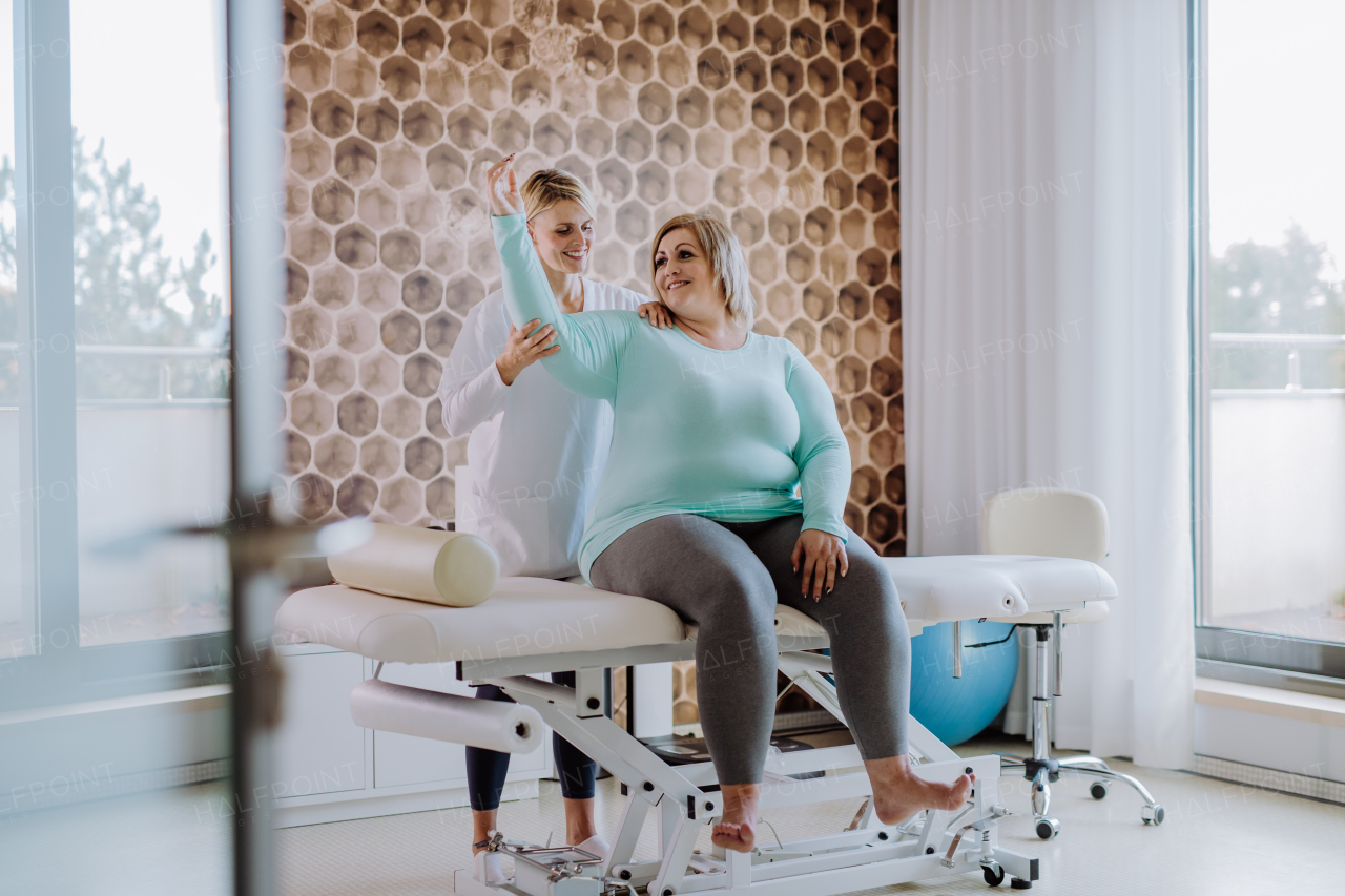 A mid adult physiotherapist woman exercising with overweight woman indoors in rehabilitation center