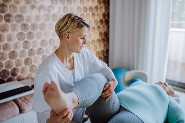 A mid adult physiotherapist woman exercising with overweight woman indoors in rehabilitation center