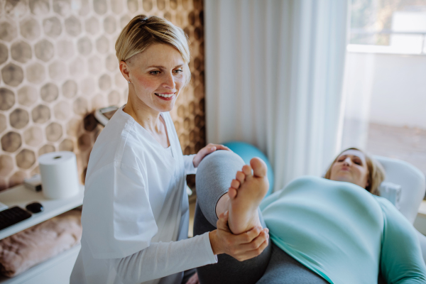 A mid adult physiotherapist woman exercising with overweight woman indoors in rehabilitation center