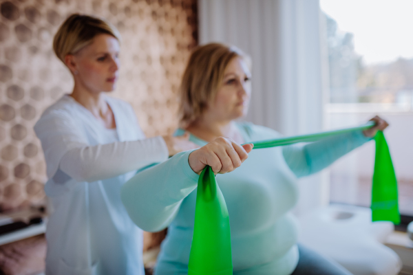 A mid adult physiotherapist woman exercising with overweight woman indoors in rehabilitation center