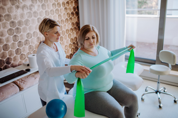 A mid adult physiotherapist woman exercising with overweight woman indoors in rehabilitation center