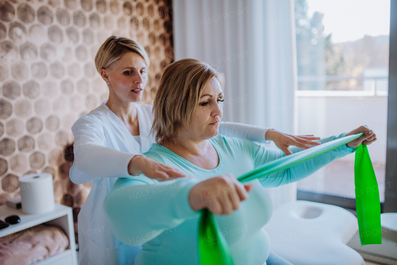 A mid adult physiotherapist woman exercising with overweight woman indoors in rehabilitation center