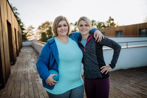 An overweight woman emracing with personal trainer outdoors on gym terrace.