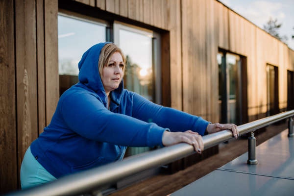 A mid adult plus size woman stretching after work out training outdoors on terrace of gym