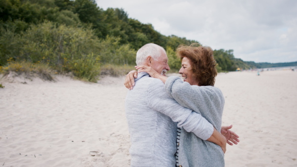 A happy senior couple in love on walk outdoors on beach at morning, hugging.