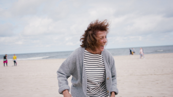 A happy senior couple in love on walk outdoors on beach at morning, running and hugging.