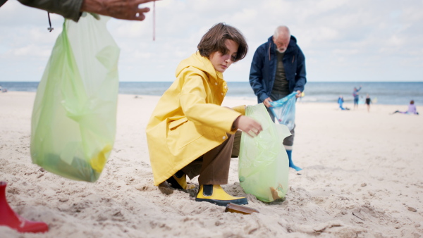 A grandparents with their granddaughter collecting garbage on beach, enviromental activists concept.