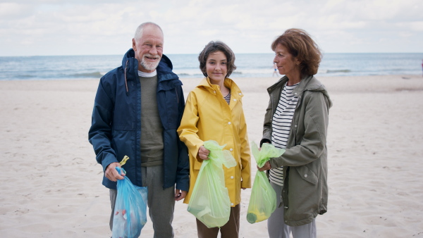 A grandparents with their granddaughter collecting garbage on beach, enviromental activists concept.