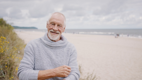 A senior man tourist loooking at camera outdoors on beach.