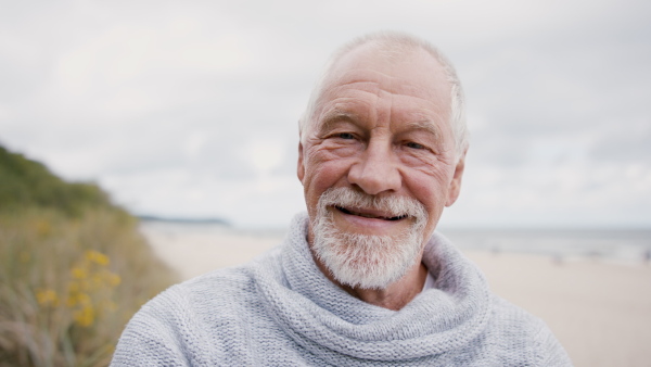 A senior man tourist loooking at camera outdoors on beach.