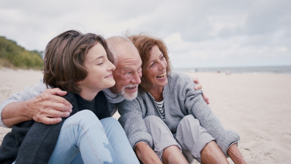 A happy grandparents with their granddaughter sitting on beach at morning and hugging.