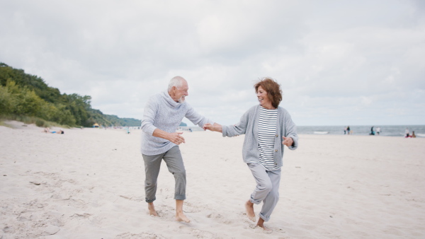 A happy senior couple in love on walk outdoors on beach at morning, running and hugging.