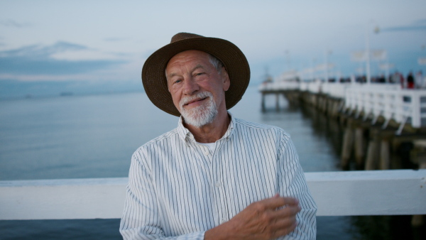 A senior man tourist loooking at camera outdoors on pier by sea.