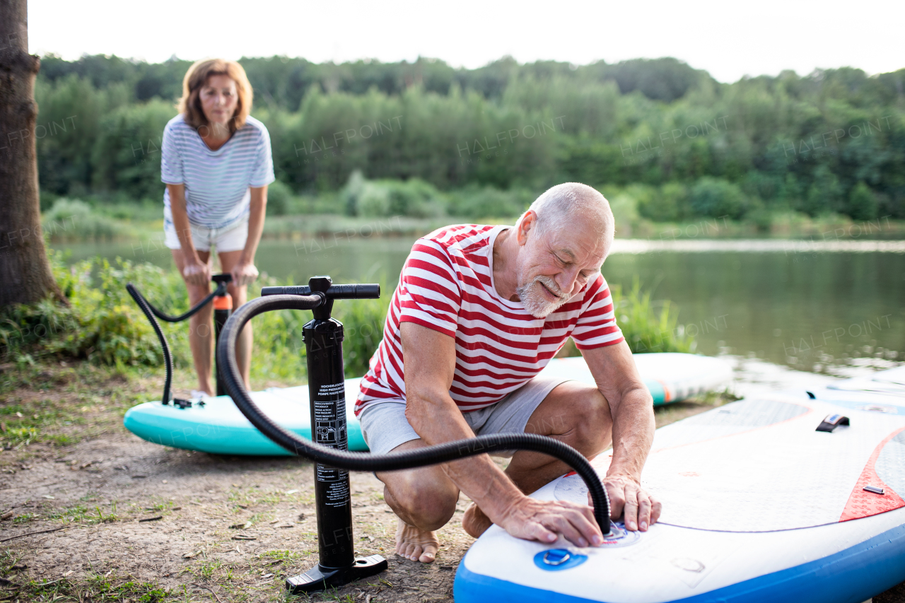 Active senior couple getting ready for paddleboarding by lake in summer.