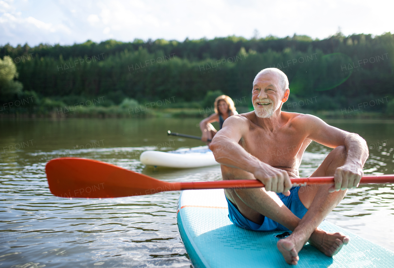 Active senior couple paddleboarding on lake in summer.