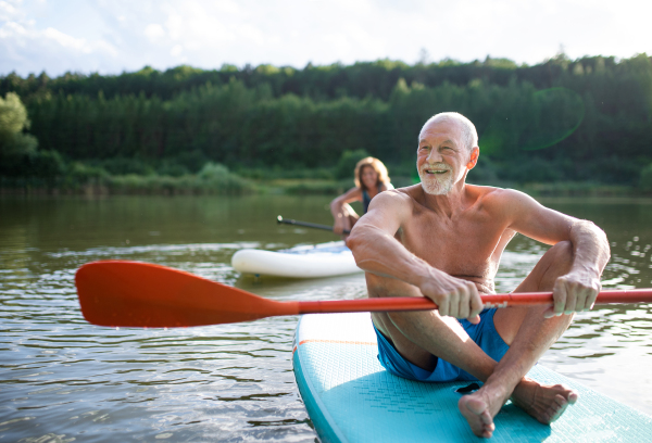 Active senior couple paddleboarding on lake in summer.