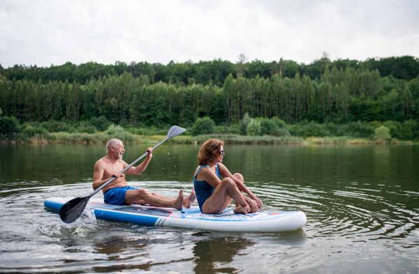 Active senior couple paddleboarding on lake in summer.