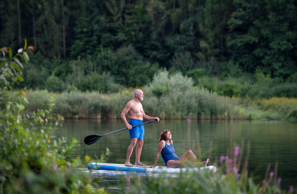 Active senior couple paddleboarding on lake in summer.