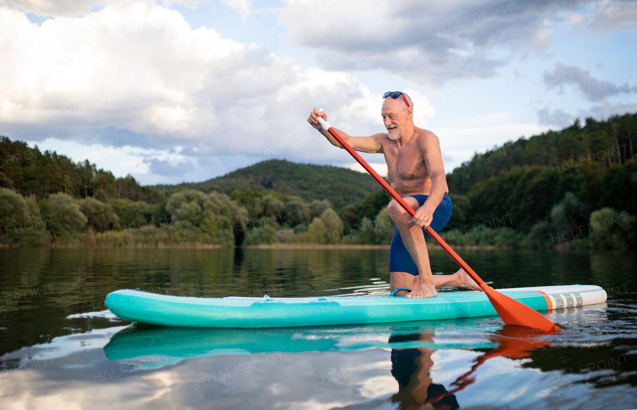 Front view of senior man paddleboarding on lake in summer. Copy space.