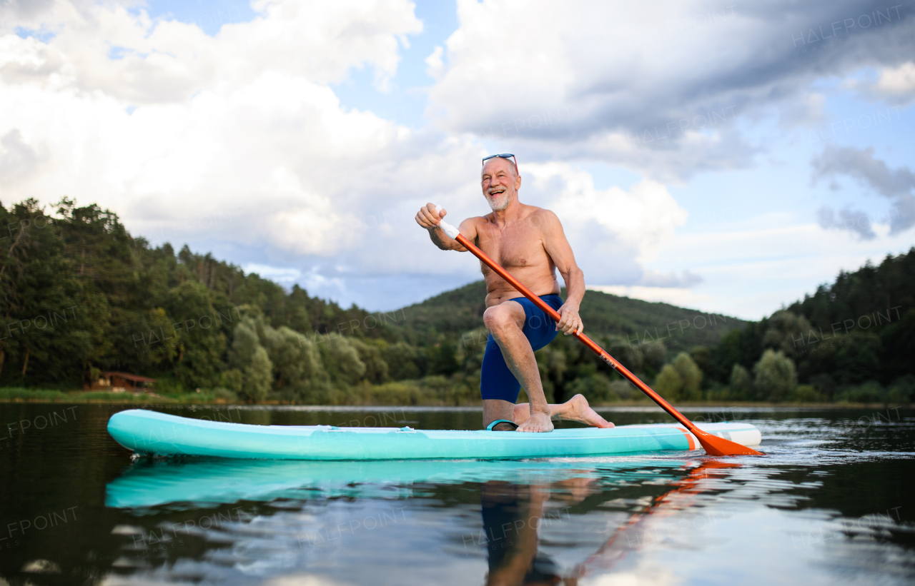 Front view of senior man paddleboarding on lake in summer. Copy space.