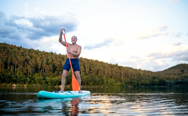 Front view of senior man paddleboarding on lake in summer. Copy space.