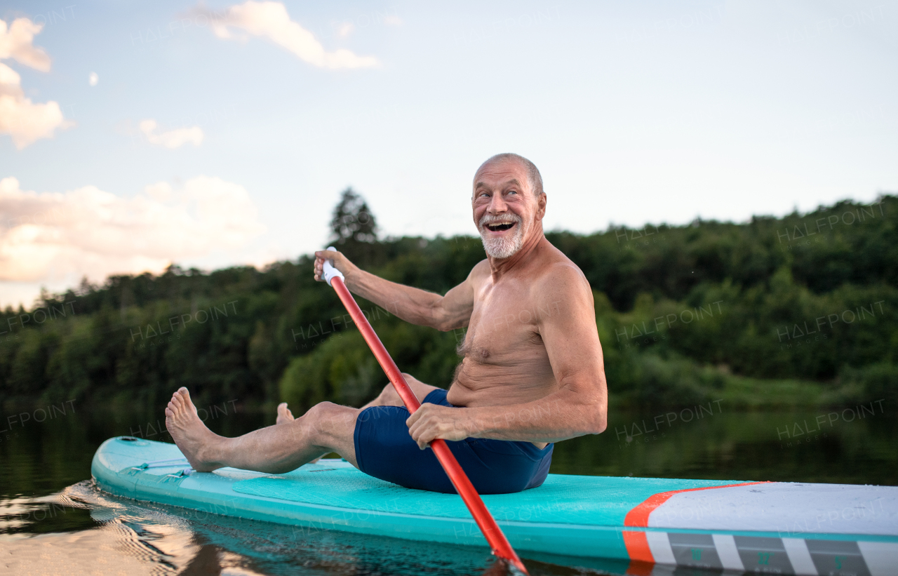 Front view of senior man paddleboarding on lake in summer. Copy space.