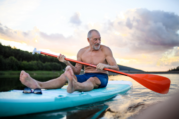 Front view of senior man paddleboarding on lake in summer. Copy space.