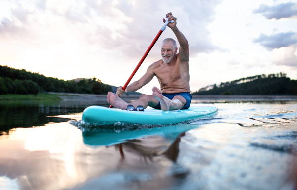 Front view of senior man paddleboarding on lake in summer. Copy space.