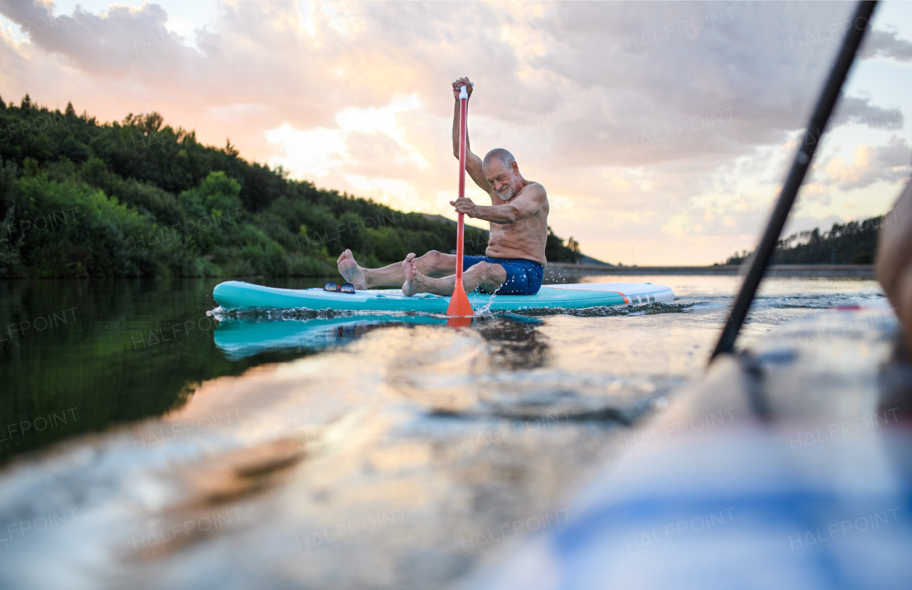 Front view of senior man paddleboarding on lake in summer. Copy space.