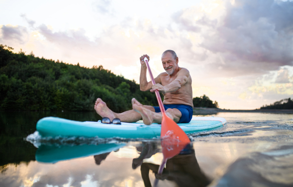 Front view of senior man paddleboarding on lake in summer. Copy space.