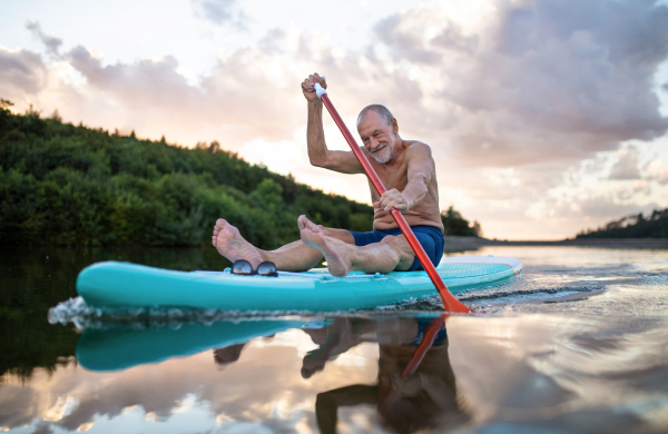 Front view of senior man paddleboarding on lake in summer. Copy space.