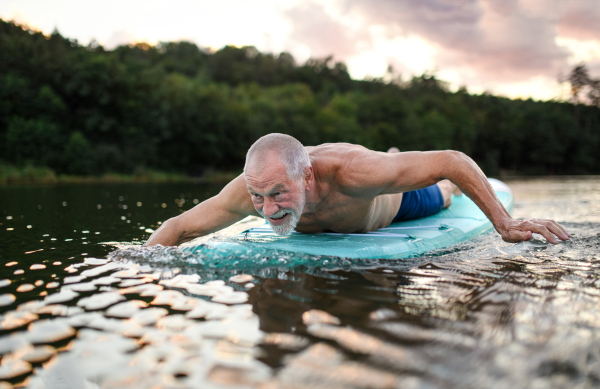 Active senior man on paddleboard on lake in summer, swimming.