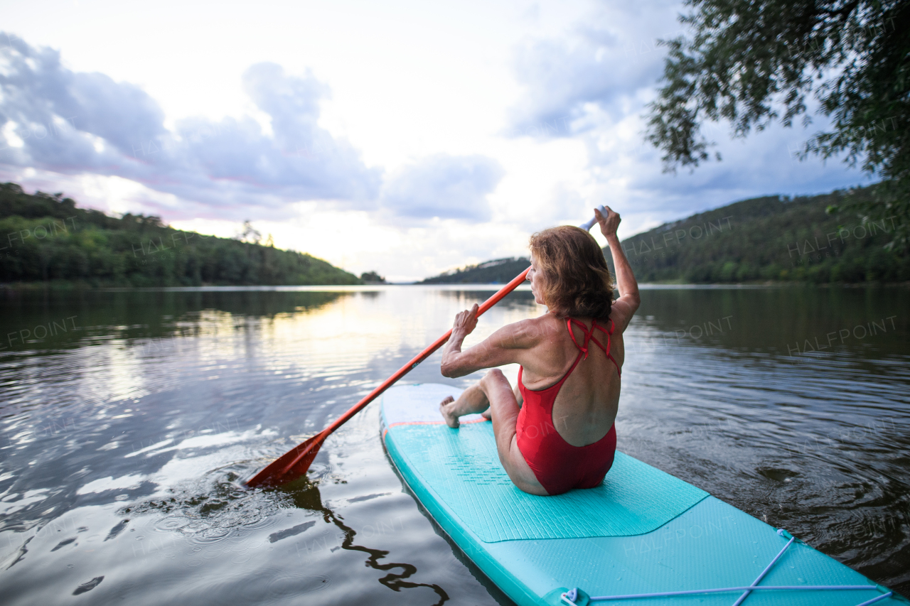 Rear view of senior woman paddleboarding on lake in summer. Copy space.