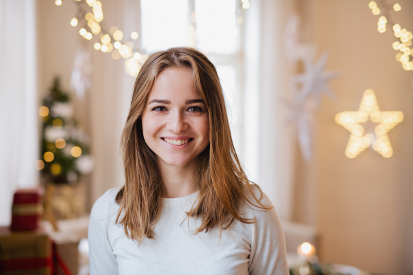 Portrait of happy young woman indoors at home at Christmas, looking a camera.