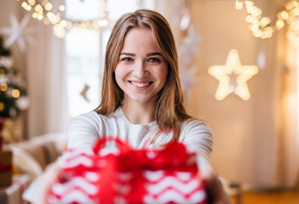 Portrait of happy young woman indoors at home at Christmas, holding present.