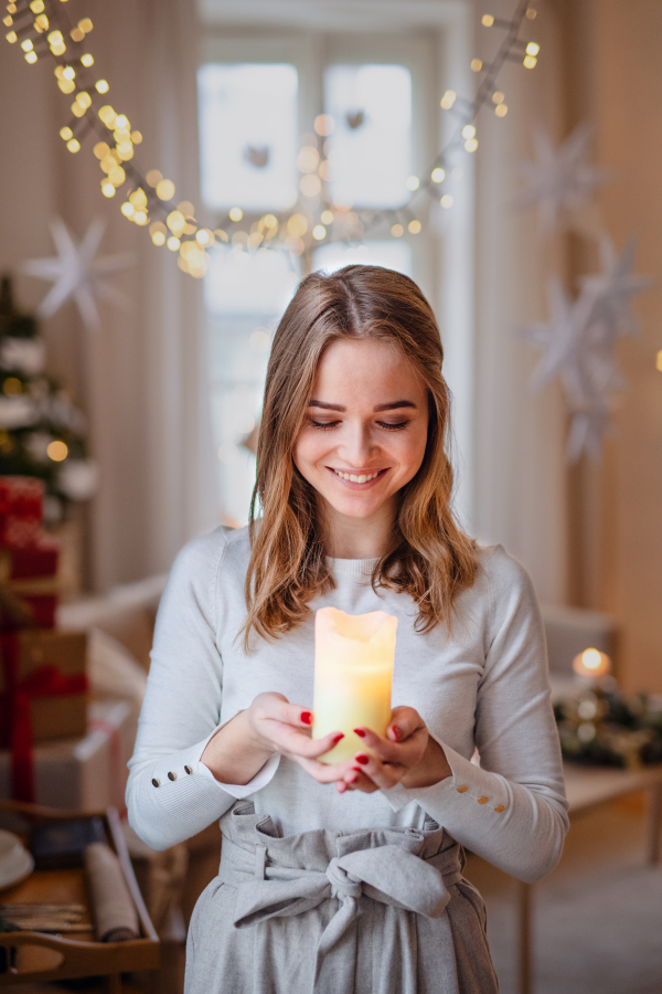 Portrait of young teenager woman indoors at home at Christmas, holding candle.