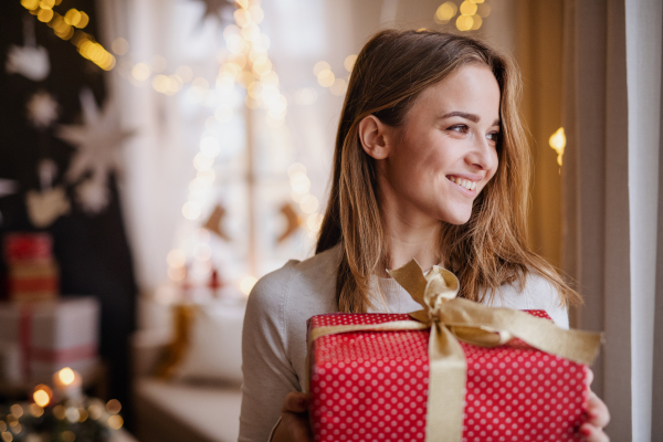 Portrait of happy young woman indoors at home at Christmas, holding present.