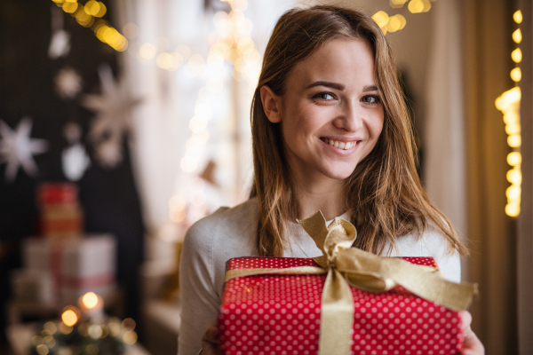 Portrait of happy young woman indoors at home at Christmas, holding present.