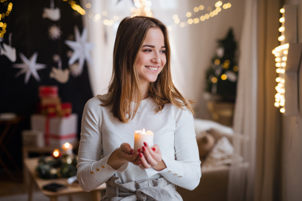 Portrait of young teenager woman indoors at home at Christmas, holding candle.