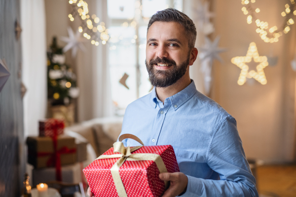 Portrait of mature man indoors at home at Christmas, holding present.