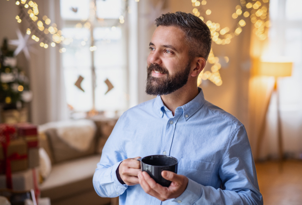 Portrait of mature man indoors at home at Christmas, holding cup of tea.