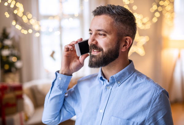 Portrait of mature man indoors at home at Christmas, using smartphone.